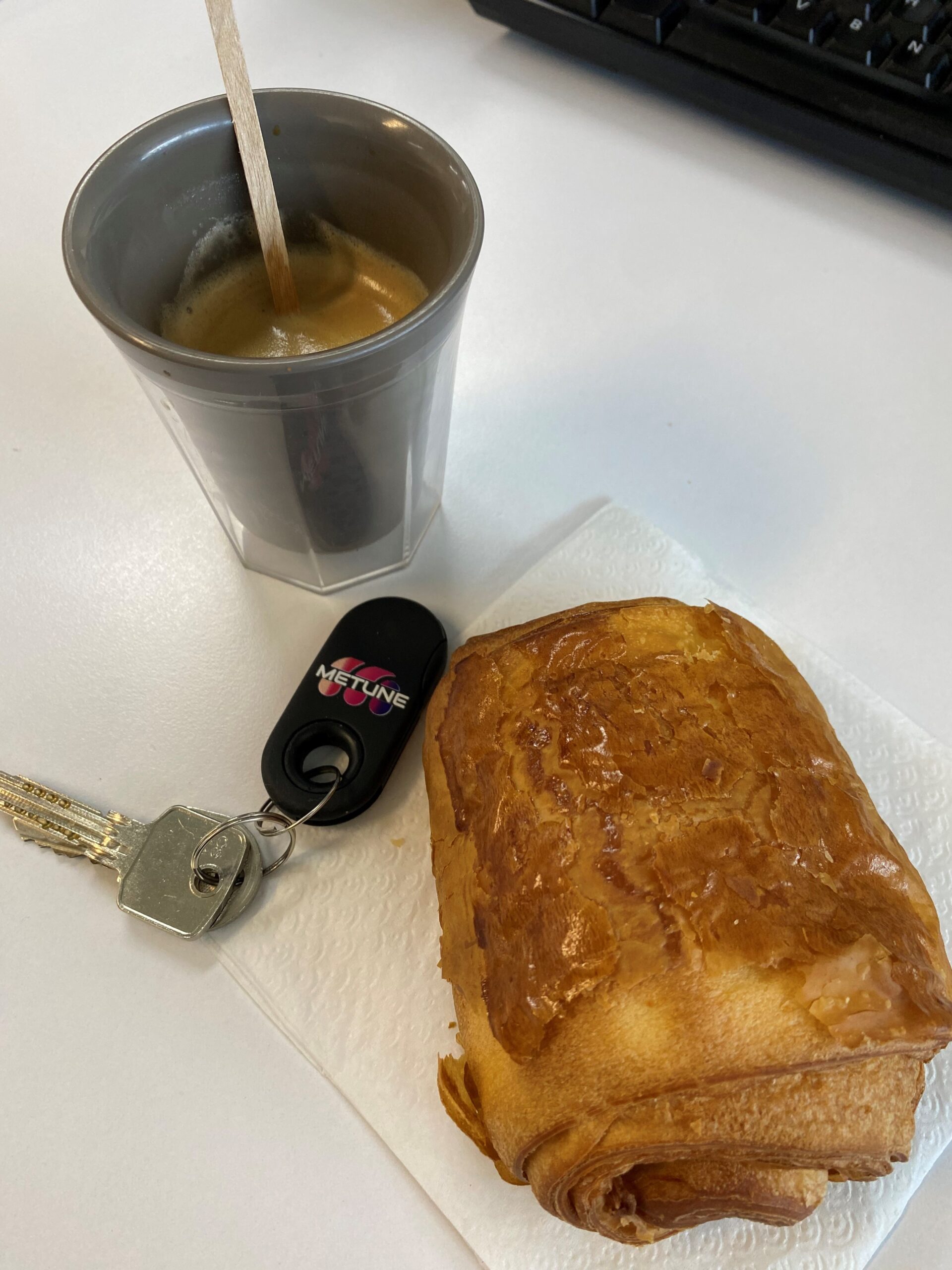 MonéClip noir avec clés à côté d’un café et pain au chocolat