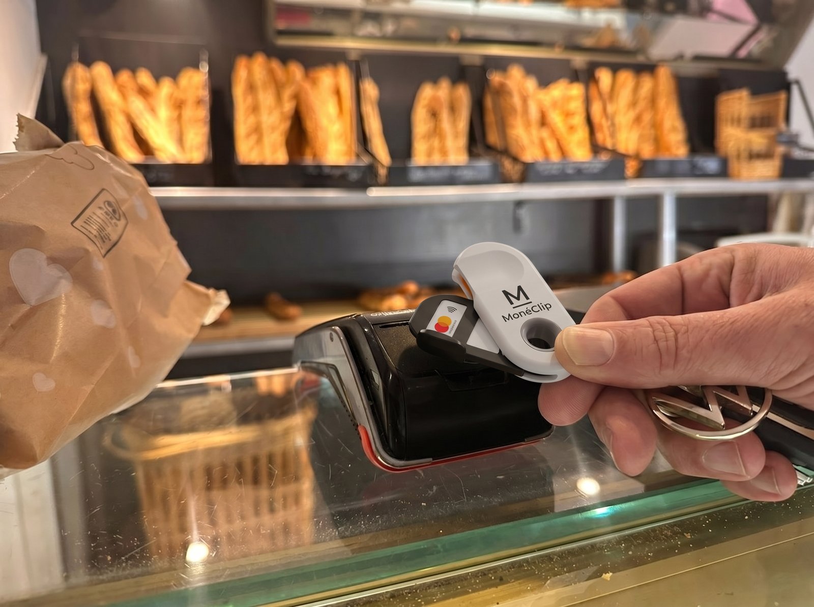 Main tenant un MonéClip sur un terminal de paiement en boulangerie